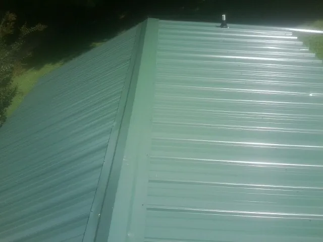 New green metal panels meeting at the ridge of a roof — Flat Roof Repair work by our crew in Hardeeville
